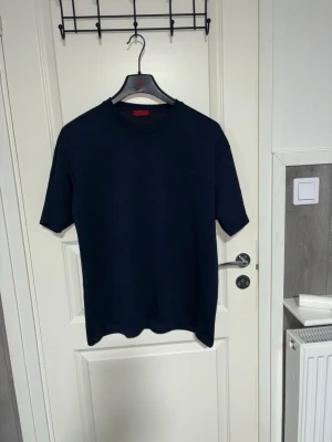 Mörkblå t-shirt från BOSS - Snygg mörkblå t-shirt från BOSS med diskret logga på bröstet. Klassisk rund halsringning och korta ärmar. Tillverkad i mjuk bomull som känns skön mot huden. Perfekt till jeans eller shorts för en clean och stilren look.