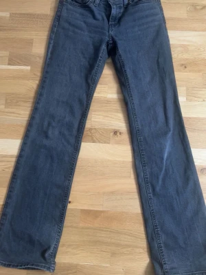 Grå bootcut jeans från Levi's - Säljer ett par grå bootcut jeans från Levi's med klassisk femficksdesign och diskret röd logotagg bak. Jeansen har normal midja och raka ben med lätt utsvängning. Perfekta för en avslappnad och trendig look.