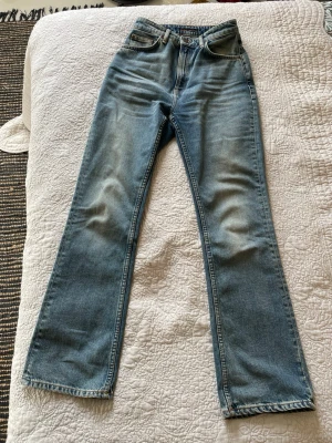 Ljusblå bootcut jeans från Nudie - Säljer ett par ljusblå bootcut jeans från Nudie Jeans med klassisk femficksmodell och snygga slitningar på framsidan. Sparsamt använda eftersom de är för stora för mig. Jag måste ha klackar då de är 5 cm för långa för mig. Jag är 160 cm.  Tillverkade i bomull. Hög midja. Framhäver kvinliga former och utsvängda ben. Riktigt snygga nu till våren.  Midjan skulle passa en tjej med stl. M. Jag är petit så passar inte mig tyvärr.  Modell Rowdry Ruth. 