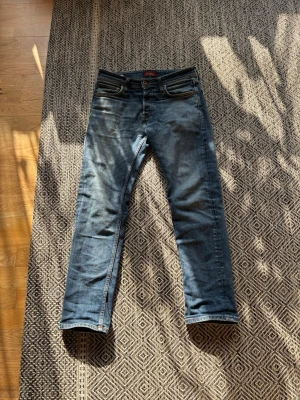 Blå raka jeans med fem fickor - Säljer ett par klassiska blå jeans med rak passform och fem fickor. Jeansen har snygga slitningar och kontrastsömmar. Materialet är denim och de har en patch bak i midjan. Perfekta för en avslappnad och trendig look. W28 L30