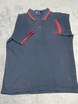 Fred Perry Polo Shirt – Dark Grey / Red Tipped – Size S - Klassisk piké från Fred Perry i mörkgrå färg med röda kontrastdetaljer på krage och ärmar.  Broderad laurel wreath-logga på bröstet.  En tidlös modell som fungerar till både jeans och chinos.  Detaljer • Fred Perry • Pikétröja • Mörkgrå / röda detaljer • Broderad logga • Storlek S • 100% bomull  📦 Skickas snabbt 💬 Skriv vid frågor