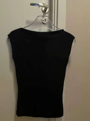 Svart ärmlös topp från Nelly XS - Snygg svart ärmlös topp från Nelly i storlek XS. Toppen har en enkel och stilren design med rund halsringning och tight passform. Perfekt att matcha med jeans eller kjol för en trendig look.