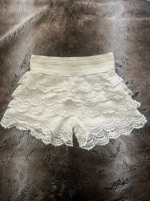 Vita spetsvolang shorts - Säljer ett par vita shorts med flera lager volang i spets. De har elastisk midja och en romantisk look med detaljerad spets som ger en bohemisk vibe. Perfekta till sommaren och riktigt snygga till både linne och crop top.