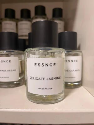 Essnce Delicate Jasmine parfym - Minimalistisk parfymflaska från Essnce med doften Delicate Jasmine. Flaskan är genomskinlig i glas med svart cylinderformad kork och vit etikett med svart text. En stilren och modern parfym som ger en fräsch jasmin-doft.