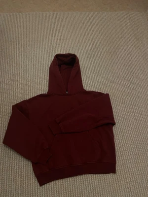 Vinröd hoodie från lager  - Mysig vinröd hoodie från lager med klassisk huva och magficka. Hoodien har ribbade muddar vid ärmslut och nederkant. Perfekt för chill dagar eller när du vill ha en enkel och stilren look.