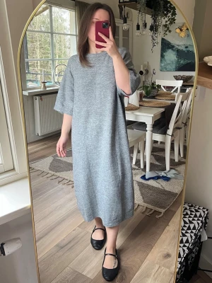 Grå stickad långklänning - Mysig grå stickad långklänning med rund halsringning och halvlånga ärmar. Klänningen har en loose passform och går att style:a till uppklätt samt nedklätt. Passar absolut L också!