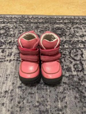 Rosa kängor från Viking med kardborre - Säljer ett par rosa kängor från Viking med två praktiska kardborreband. Skorna har en kombination av slätt och mockaliknande material, samt robust svart sula. Perfekta för kalla dagar och lätta att ta på och av.