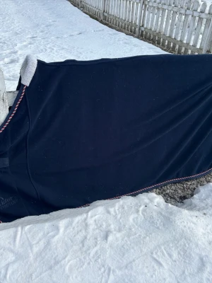 Marinblå fleecetäcke Rider's Company - Säljer ett marinblått fleecetäcke från Rider's Company. Täcket har broderad logga och snygg kant i rött, vitt och blått. Perfekt för häst och utrustad med mjukt material som håller värmen. Passar bra till kalla dagar i stallet.