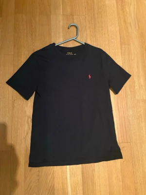 Svart t-shirt från Polo Ralph Lauren - Klassisk svart t-shirt från Polo Ralph Lauren med den röda logotypen broderad på bröstet. Storlek 12 (150). Köpt på Kids Brand Store, nypris 595kr.