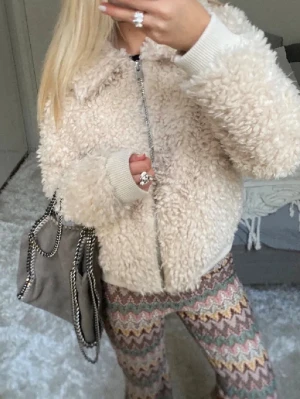 Fluffig och vårig teddyjacka! - Supermysig teddyjacka i krämvit färg med fluffig struktur och dragkedja framtill. Jackan har ribbade muddar vid ärmslut och nederkant samt en klassisk krage. Perfekt för att hålla värmen och ge en trendig look nu till våren! Skriv för frågor och innan ni köper, INTE MINA BILDER!! Skriv för egna bilder ❤️Pris kan diskuteras!