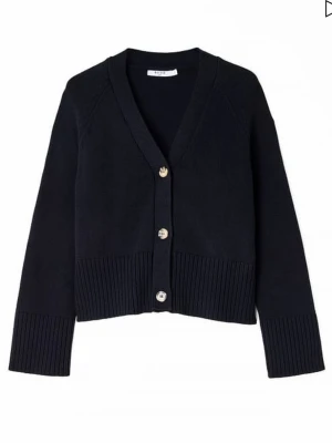 Svart ribbad kofta med knappar - Stilren svart kofta med v-ringning och tre stora knappar framtill. Koftan har breda ribbade muddar vid ärmslut och nederkant, samt en något boxig och croppad passform. Perfekt att slänga över en t-shirt eller linne för en chill look.