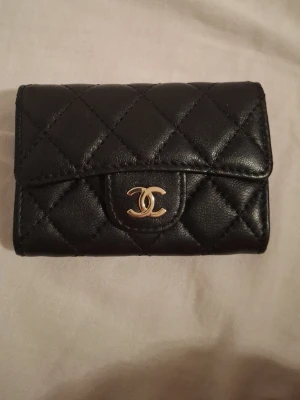 Svart quiltad plånbok  - Säljer en svart quiltad plånbok . Plånboken har klassiskt rutmönster l. Perfekt storlek för kort och kontanter, med elegant och tidlös design.