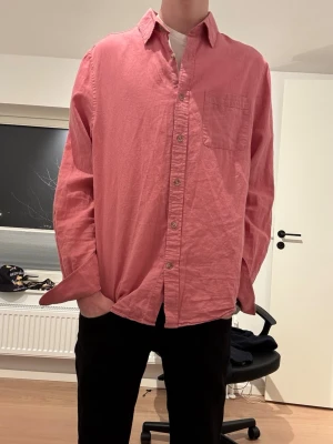 Rosa linneskjorta från Dressmann - Säljer en snygg rosa skjorta från Dressmann i linnemix. Skjortan har klassisk krage, bröstficka och knappar framtill. Passformen är loose och materialet känns luftigt och skönt, perfekt för dig som gillar en avslappnad stil. Kika gemensamma annonsen om du söker fler skjortor till våren eller sommaren! Hör av er vid eventuella frågor