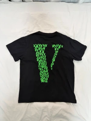 Vlone playboi carti- Medium - Svart t-shirt från Vlone x Playboycarti tröja med grönt Playboy-kanintryck på bröstet och stor grön V-logga på ryggen. Klassisk passform och rund hals. Perfekt statement-plagg för dig som gillar streetwear och unika samarbeten.