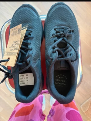 Svarta Nike sneakers med komfortsula - Snygga svarta sneakers från Nike med komfortsula och stickad ovandel. Skorna har klassisk snörning, diskret Nike-logga på sidan och en slitstark sula med bra grepp. Tillverkade med minst 20% återvunnet material. Perfekta för en aktiv vardag och streetstyle.
