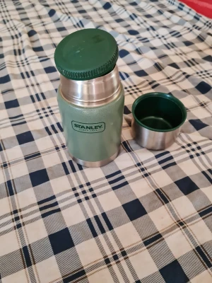 Grön termos från Stanley - Säljer en klassisk grön termos från Stanley i rostfritt stål med grönt lock och tillhörande kopp. Perfekt för att ta med varm dryck på utflykten. Termosen har en robust design och rymmer lagom mycket för en person.