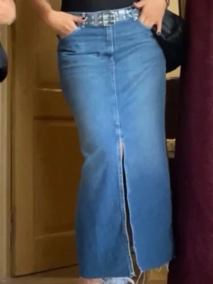 Lång jeanskjol med slits - Trendig lång jeanskjol i blå denim med hög midja och framslits. Klassisk femficksmodell med rå kant nertill för en cool look. Perfekt att styla med bälte och sneakers.
