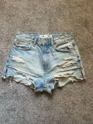 Ljusblåa denimshorts med slitningar - Snygga ljusblåa denimshorts från New Yorker. Shortsen har flera slitningar framtill och klassisk femficksdesign. Storlek XS. Mid waist.