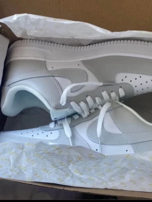 Nike Air Force 1 '07 vita sneakers - Nike Air Force 1 '07 i helvitt läder med klassisk siluett och perforerade detaljer på tån. Skorna har vit sula, vita skosnören och den ikoniska swoosh-loggan på sidorna. Perfekta för en clean och stilren look.