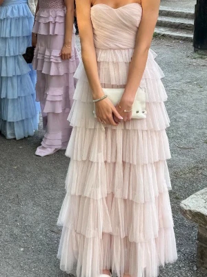 Ljusrosa långklänning med volanger - Säljer min superfina balklänning med flera lager volanger. Det finns även band som går och knyta över axlarna! Skriv om fler bilder då dessa bilder är endast från min bal💗