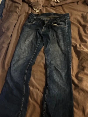 Mörkblå raka jeans SÖKES - Säljer ett par mörkblå jeans med klassisk rak passform och fem fickor. Jeansen har snygga slitningar och kontrastsömmar. Perfekta till en avslappnad stil och funkar året runt.