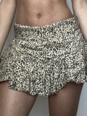 Leopardmönstrad volangkjol - Säljer en kort kjol med leopardmönster och volangdetaljer. Kjolen har en beige bas med svarta och bruna fläckar och är perfekt för dig som vill sticka ut. Den har en figurnära passform i midjan och är lätt och luftig.