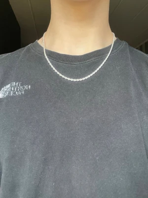 Silverpläterat halsband från Indossa - Säljer ett stilrent halsband i silverfärg med tvinnad kedja. Halsbandet har en enkel och clean design som passar perfekt till många olika outfits. Materialet är metall och kedjan har en snygg glansig finish.