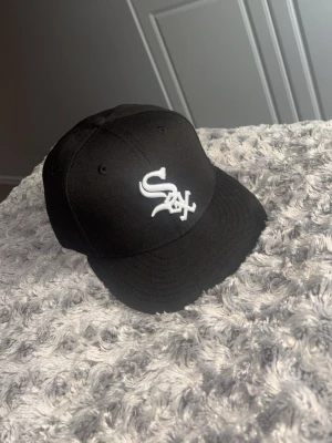Svart White Sox keps från New Era - Säljer en svart keps från New Era med White Sox-logga broderad i vitt framtill. Klassisk böjd skärm och MLB-logga baktill. Kepsen är i ett stilrent utförande och passar perfekt till streetwear-looken.
