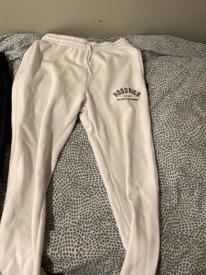 Vita mjukisbyxor från Hoodrich - Snygga vita mjukisbyxor från Hoodrich med tryckt logga på vänster lår. Byxorna har resår i midjan med dragsko och är tillverkade i mjukt material för maximal komfort. Perfekta för en avslappnad och trendig stil.