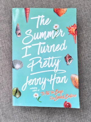 The Summer I Turned Pretty - En ungdomsroman på engelska med turkos mjukpärm, dekorerad med färgglada snäckor och blommor. Boken handlar om sommarlov, vänskap och kärlek på Cousins Beach. Perfekt för dig som gillar romantik och coming-of-age berättelser.