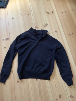 Massimo dutti mörk blå långärmad  - Snygg mörkblå tröja med hög krage och knappar framtill från Massimo dutti. Tröjan har långa ärmar och förstärkta armbågslappar för en cool detalj. Ribbstickade muddar vid ärmslut och nederkant ger en skön passform. Perfekt för lager på lager och stilrena outfits. Passar dig som är runt 170cm