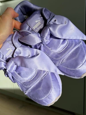 FENTY x PUMA sneakers – lila satin / Rihanna (stl 38) - Säljer ett par stilrena FENTY x PUMA by Rihanna sneakers i lila med sidenliknande finish Den klassiska modellen med breda band/rosetter – en ikonisk design från Rihanna-kollektionen. Storlek: 38 Original från PUMA Skorna är använda och har synligt slitage (se bilder), särskilt på tygytan och framtill.  De är dock fortfarande fullt användbara och passar perfekt som vardagsskor eller för dig som gillar modellen. Perfekta som extra skor, festival eller vardag också