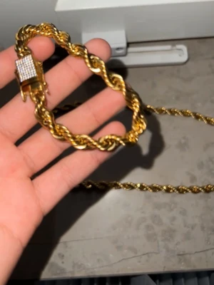 Guld armband  - Snyggt guldfärgat armband med tvinnad kedja och ett lås dekorerat med små diamanter  stenar. Armbandet har en robust känsla och passar perfekt för att ge din outfit. De är guld. Planterad och är rosfristond. 8 mm Pris. Kan diskuteras 