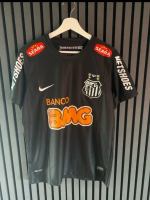 Svart Santos FC Neymar matchtröja - Snygg svart matchtröja från Santos FC med Neymar Jr och nummer 11 på ryggen. Tröjan har tryckta sponsorer som BMG, Seara och Netshoes samt klubbmärke på bröstet. Tillverkad i lätt och ventilerande material, perfekt för fotbollsträning eller support.