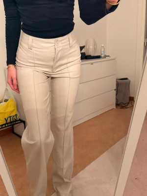 Beiga läder/skinn byxor - Snygga beiga jeans från Amisu med hög midja och raka ben. Byxorna har markerade sömmar framtill som ger en trendig look. Perfekta att styla med en enkel topp eller stickad tröja.