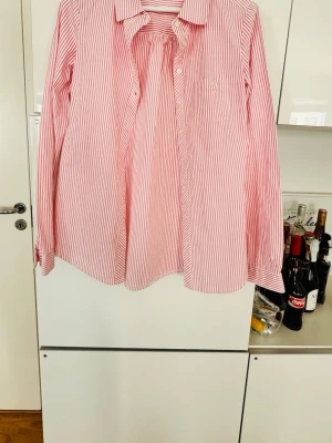 Randig rosa skjorta från Vila - Säljer en långärmad skjorta från Vila med rosa och vita ränder. Skjortan har klassisk krage, knappar framtill och en bröstficka. Materialet är mjukt bomull och passformen är normal. Perfekt för dig som gillar en clean och fräsch look.