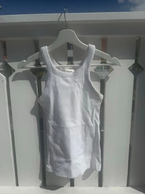 Vit ribbad linnetopp - Säljer en klassisk vit ribbad linnetopp med rund halsringning och smala axelband. Perfekt att styla till jeans eller shorts för en enkel och fräsch look. Materialet är mjukt och stretchigt för en bekväm passform.
