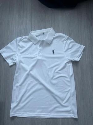 Vit pikétröja från Ralph Polo - Klassisk vit pikétröja från Ralph Polo med krage och korta ärmar. Tröjan har knappar vid halsen och en liten broderad logga på bröstet. Tillverkad i ett mjukt och lätt material som passar perfekt till sommaren. Storleken är M och den kan även sitta som S. Aldrig använd pga att den är för liten för mig