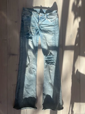 Ljusblå slitna bootcut jeans Cheap Monday - Säljer ett par ljusblå bootcut jeans från Cheap Monday med slitningar och hål på låret och knät gjort själv. storlek 26/32❣️