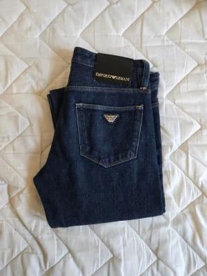 Mörkblå jeans från Emporio Armani - Snygga orginal mörkblå jeans från Emporio Armani med klassisk femficksdesign och silverfärgad logga på bakfickan. Jeansen har raka ben och är tillverkade i mjukt denimtyg som ger en stilren och tidlös look. Testade nångång så som helt nya