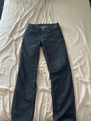 Mörkblå jeans från Nudie Jeans - Säljer ett par mörkblå raka jeans från Nudie Jeans. Klassisk femficksmodell med orangea sömmar och logga på bakfickorna. Jeansen är i 100% bomull och har en snygg, stilren look som passar till det mesta. Rad rufus 29 32 tvättas en gång innan försäljning, 50 wears ungefär