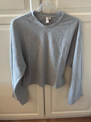 Grå långärmad topp från Nelly - En enkel och stilren grå långärmad topp från Nelly. Toppen har rund halsringning och är tillverkad i ett mjukt material som känns skönt mot huden. Storlek M. I fint skick.