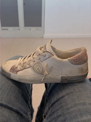Philippe Model vita låga sneakers - Snygga vita sneakers från Philippe Model med lågt skaft och klassisk design. Skorna har mockadetaljer runt hälen och logotyp på sidan. Materialet är en mix av läder och mocka, med röda broderade detaljer på hälen. Perfekt för dig som gillar stilrena sneakers. Skriv till mig innan tackkk