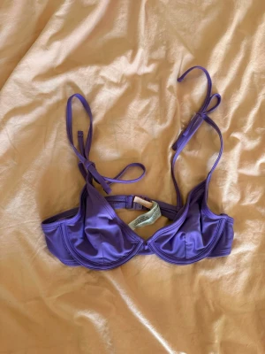 Lila bikiniöverdel med knyt - Snygg lila bikiniöverdel med bygel och knytbara axelband. Modellen har en klassisk balconette-form som ger bra stöd och en trendig look. Perfekt för stranden eller poolen. Materialet känns mjukt och följsamt mot huden. Endast provad. Obs katt finns i hem!