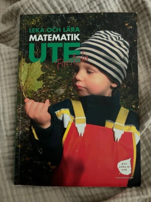 Leka och lära matematik ute - Boken 'Leka och lära matematik ute' ger inspiration till matematikövningar utomhus för förskolebarn. Innehåller lekar, sorteringsövningar och aktiviteter med naturtema. Omslaget är grönt med ett foto på ett barn i färgglada kläder. Perfekt för pedagoger och naturintresserade.