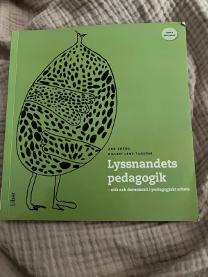 Lyssnandets pedagogik kursbok - Kurslitteratur: 'Lyssnandets pedagogik – etik och demokrati i pedagogiskt arbete' av Ann Åberg och Hillevi Lenz Taguchi. Boken har ett grönt mjukt omslag med svart illustration och är skriven på svenska. Perfekt för dig som pluggar pedagogik eller förskollärarutbildning.
