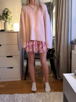 Ljusrosa oversized stickad tröja - Mysig ljusrosa stickad tröja med oversized passform och rund hals. Tröjan har långa ärmar och ribbstickade muddar vid ärmslut och nederkant. Perfekt att styla med både kjol och jeans för en avslappnad look.