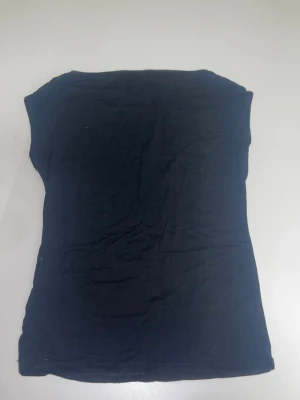 Svart ärmlös t-shirt i bomull - En svart ärmlös t-shirt i mjuk bomull med enkel och rak passform. T-shirten har en klassisk look utan synliga detaljer eller mönster, vilket gör den lätt att styla till olika outfits.