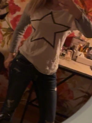 Vit topp med stjärntryck - Vit långärmad topp med grå ärmar och stor svart stjärna framtill. Skön och avslappnad passform, perfekt till jeans. Materialet känns mjukt och stretchigt, troligen bomull eller polyesterblandning.