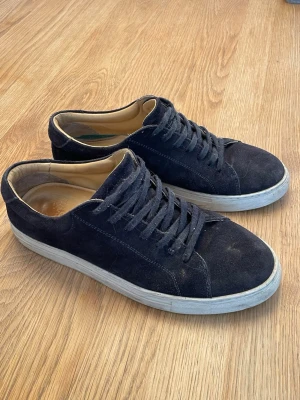 Myrqvist skor - Mörkblå Myrqvist sneakers i mocka med klassisk låg profil och vita sulor. Ljusbeige insida, matchande mörkblå skosnören och en enkel stilren design. Inga stora defekter som hål, bara små slitningar här o där. Strl 42.                                    Box ingår!